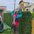 Person trimming a hedge using a power tool in a residential area.