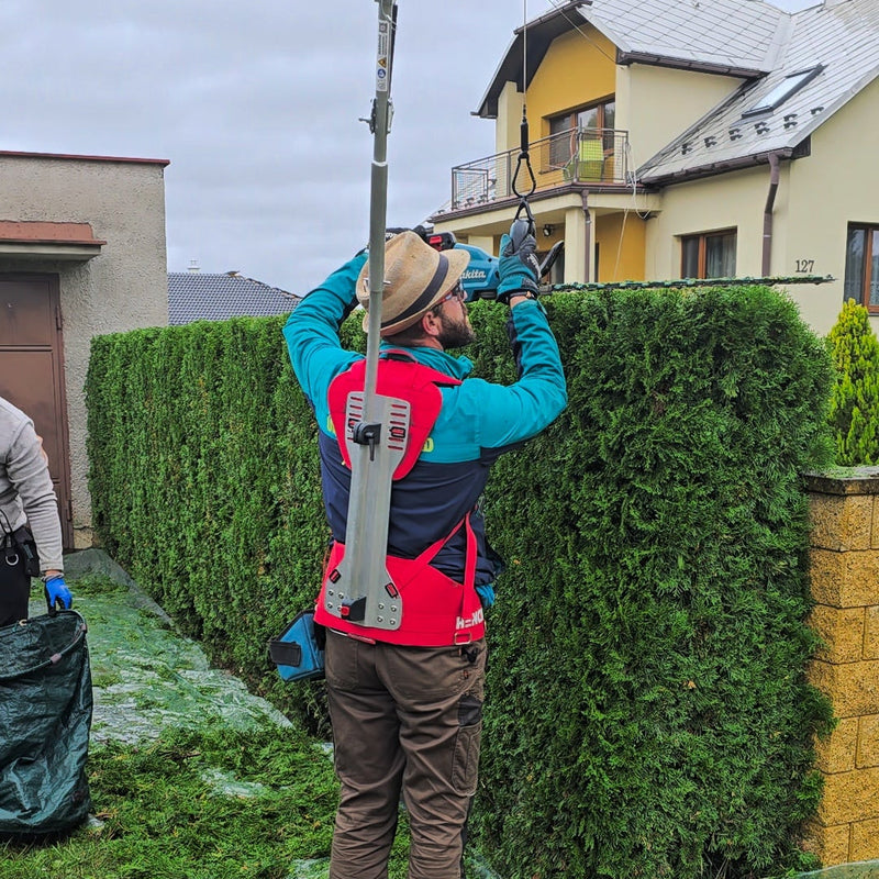 Person trimming a hedge using a power tool in a residential area.